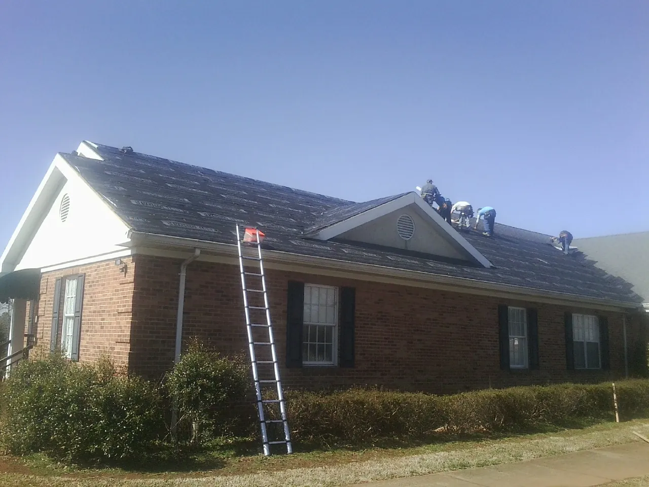 Crew tearing shingles off a brick ranch roof with a ladder set — Emergency Roof Repair work by our crew in Nashua
