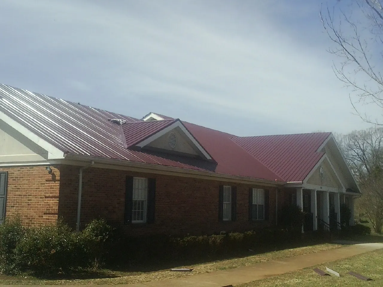 Red metal roof with gabled entries on a long brick building, from a Hail Damage Roof Repair job in Nashua