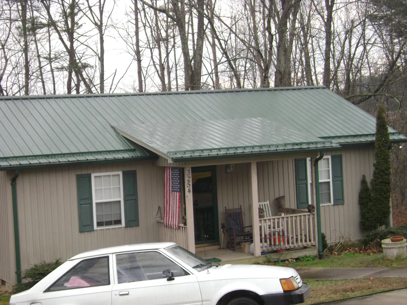 Green metal roof and front porch on a tan sided cottage in Nashua