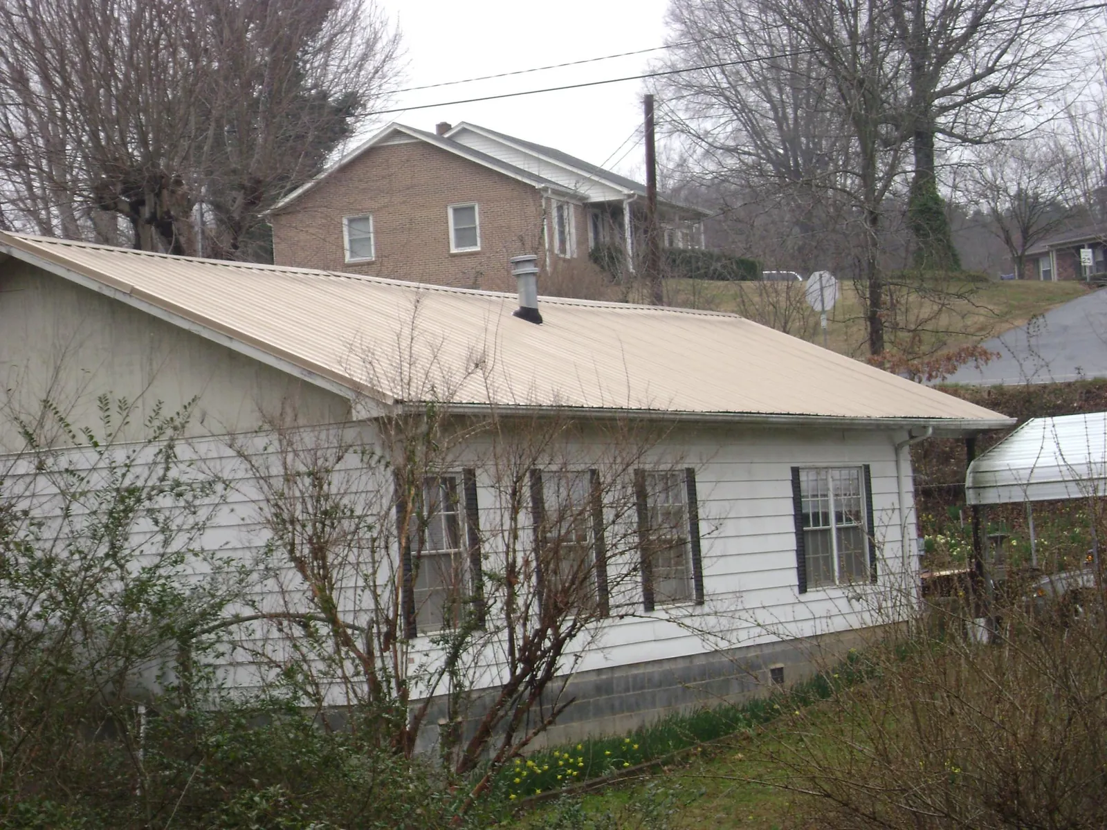 Tan metal roof on a white sided house set into a hillside — Commercial Roofing by Roofing Brothers in Nashua